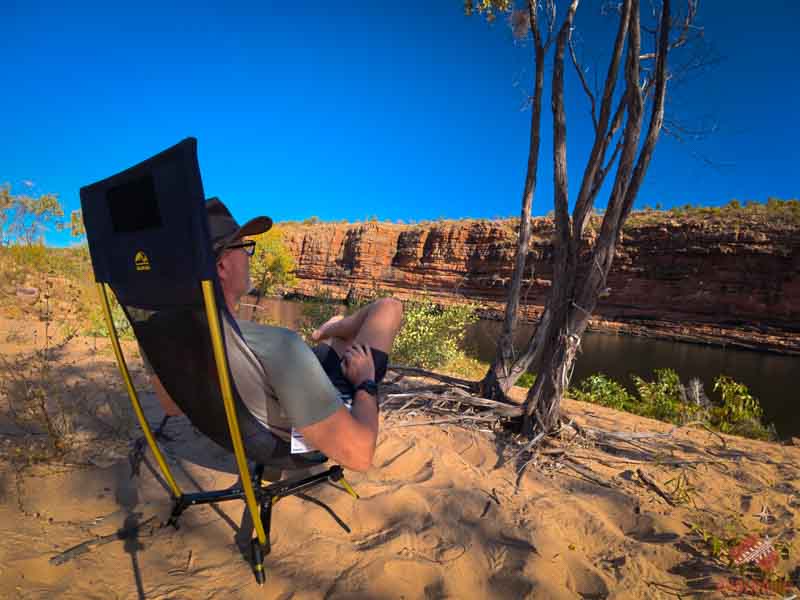 Stephan in a Kilos High Peak chair at Camera Pool, with red cliffs and the river behind